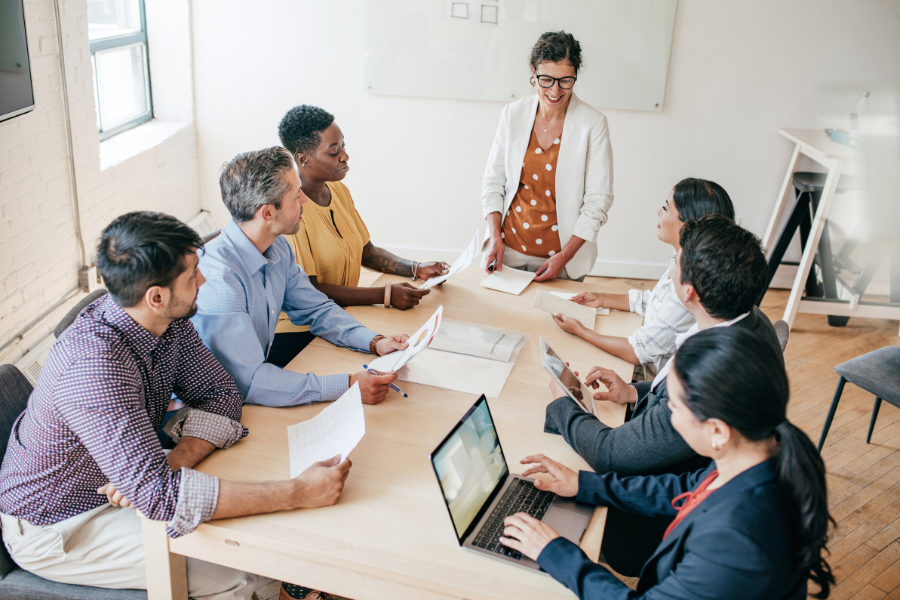 Group of colleagues around a conference table reviewing documents as a woman leads the discussion.