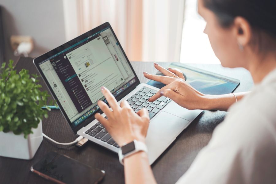 Person typing on a laptop at a desk with a chat app open on the screen and a plant nearby.